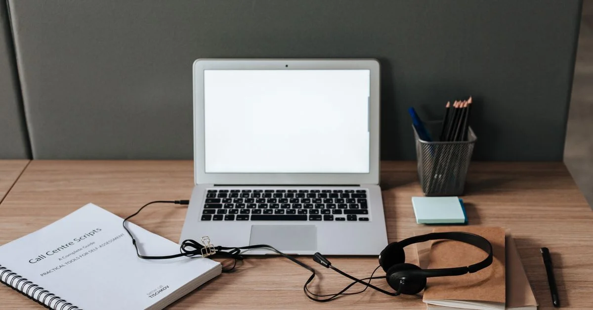 Espace de travail minimaliste avec ordinateur portable, casque et scripts de centre d'appels sur un bureau en bois.