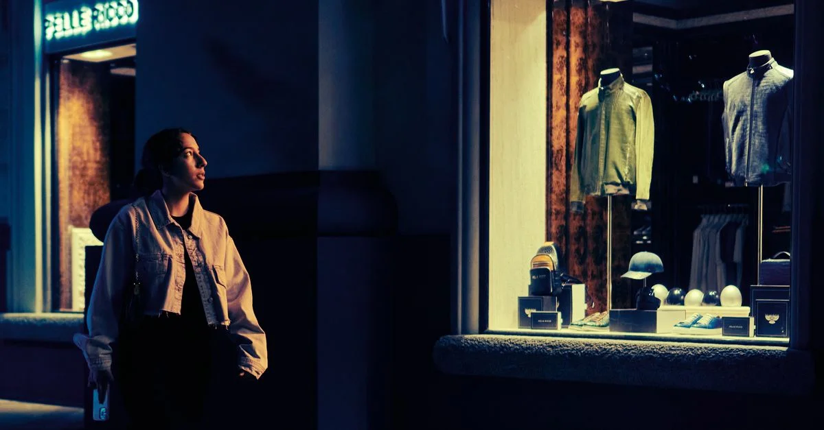 Une femme regardant une vitrine éclairée dans un cadre urbain la nuit.
