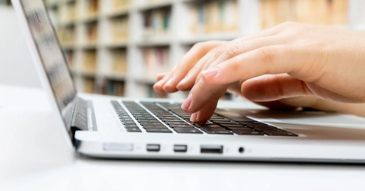 Gros plan sur des mains tapant sur un clavier d'ordinateur portable dans une bibliothèque.