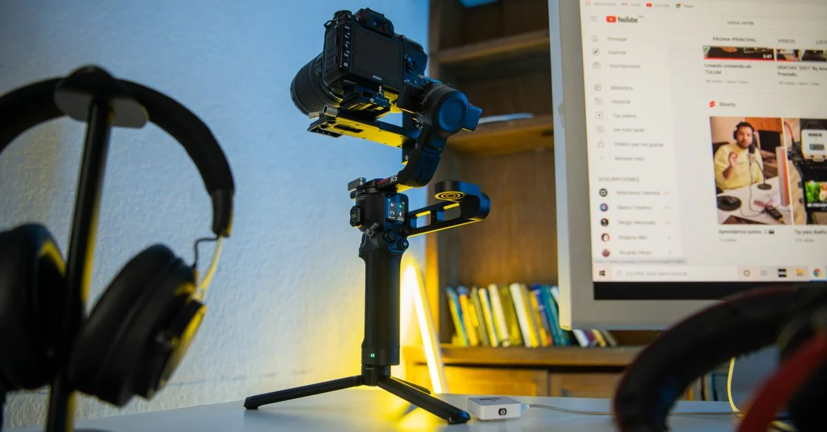 Configuration de photographie professionnelle avec un appareil photo sur trépied, un casque et un moniteur d'ordinateur affichant du contenu vidéo.