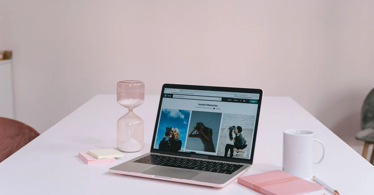 Un espace de travail propre et minimaliste avec un ordinateur portable, un sablier, un bloc-notes et une tasse de café sur un bureau blanc.