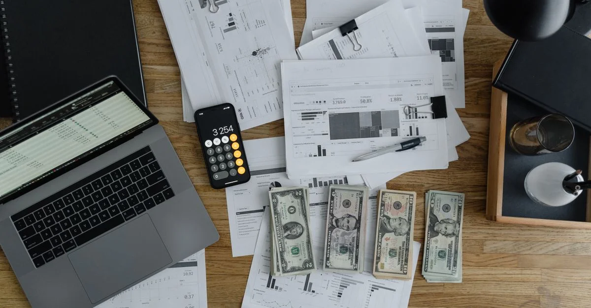 Vue de dessus de documents financiers, de billets et de technologie sur un bureau en bois.